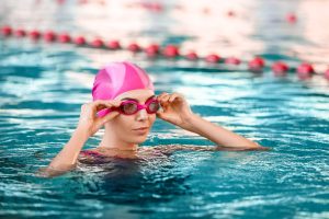 Benefici del nuoto: perché è uno degli sport più completi donna in piscina con la cuffia rosa, sta indossando gli occhiali felice dei benefici del nuoto